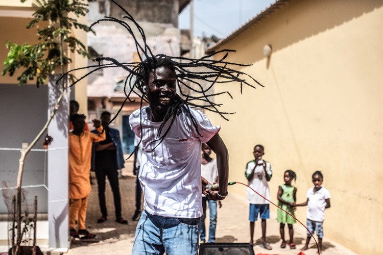 A man holds a microphone behind him and his dreadlocks fly around him. He is smiling.