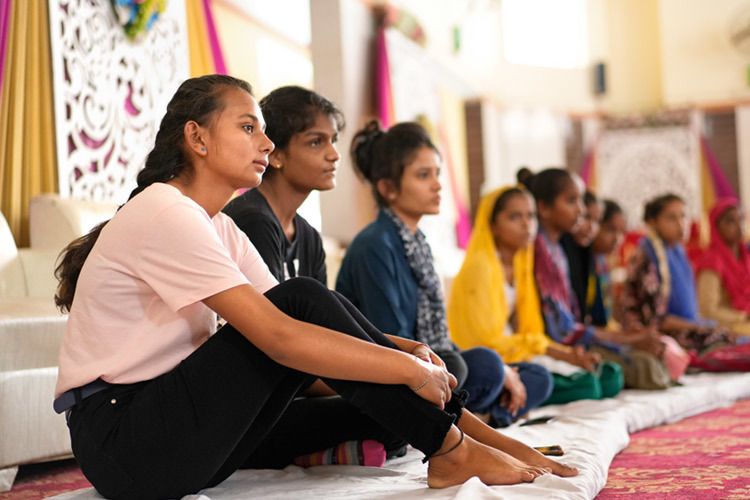 Neeraj sits on the floor looking away from the camera with other young women. She was photographed at AMIED's workshop in Kishangarhbaas, India, August 2022. Photo by Deepak Sharma.