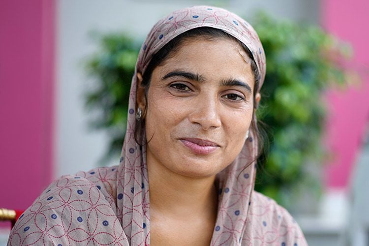 Zara, a young woman smiling and wearing a pink head scarf, was photographed at AMIED's workshop in Kishangarhbaas, India, August 2022. Photo by Deepak Sharma.